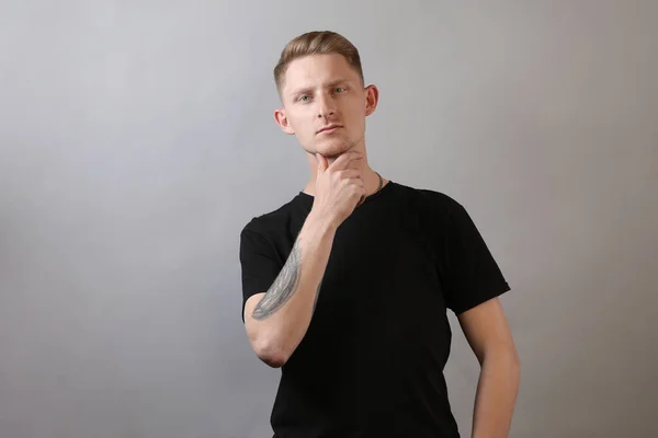 Portrait of young handsome man with style hairdo in casual black t-shirt with arm crossed looking at camera and grinning at studio isolated on gray background. Natural expression. copy space.