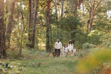 Parkta evcil hayvanlarla koşan neşeli bir aile. Genç anne, baba üç çocuk ve büyük köpekle dışarıda eğleniyor. Çocuklu aileler el ele tutuşuyor. Aktif yaşam tarzı ebeveynlik kavramı. Mutlu çocukluk.