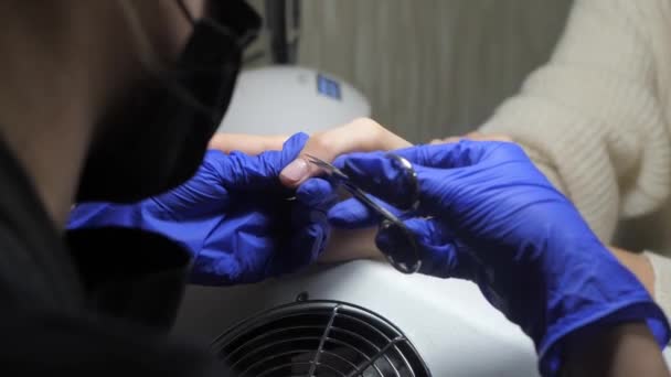 指甲长在蓝色橡胶手套中 为指甲的修整准备指甲 美容院美容师用专业的金属仪器切割角质层 用剪刀去除角质层 — 图库视频影像