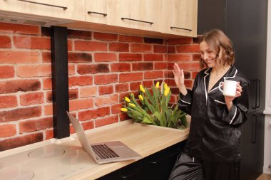 Concentrated attractive young woman in home cloth, housewife preparing and cooking food and mixing in frying pan on induction stove for delicious dinner at modern loft style kitchen. Advertising