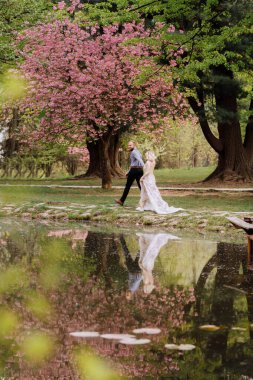 Valentines day. Beautiful, cheerful and lively newlyweds, groom and bride are hugging near the blooming pink cherry blossom. Wedding portrait of a close-up of a smiling bearded groom and a cute bride