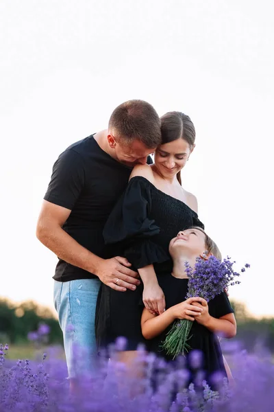happy family day. Young mother, father and little daughter in purple lavender field. Dad, mom and child hugging and looking on each others on nature on summer. Concept of friendly family. family look.