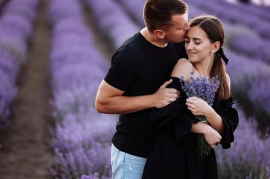 Gün batımında mor lavanta tarlasında kucaklaşan sevgi dolu çift. Güzel genç insanlar yaz sıcağında buluşur ve dışarıda birlikte yürürler. Aşk kavramı. İki kişilik genç bir aile.