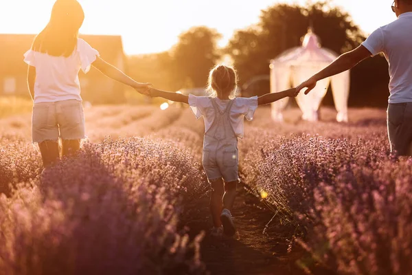 happy family day. young father, mother and child daughter are having fun together in the lavender field and looking at each other. happy couple with kid enjoy summer holiday vacation. family look.