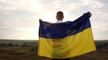 Vatanseverliğin göstergesi olarak sırt üstü mavi ve sarı Ukrayna bayrağını gururla taşıyan adamın arka görüntüsü. Ukrayna 'daki Rus savaşını protesto etmek, silahlı çatışma, evsiz, kriz, portre
