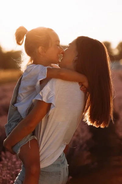 family day. young mom and little daughter enjoy relaxing in a field with lavender at sunset. A beautiful mother hugs and kiss child girl tightly. Maternal care and love for the child. mothers day.