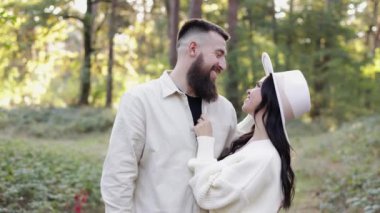 St. Valentines day. Happy stylish loving couple hugging and looking to each others in sunny park. Young bearded man and woman in hat are having date or celebrating anniversary and enjoying nature.