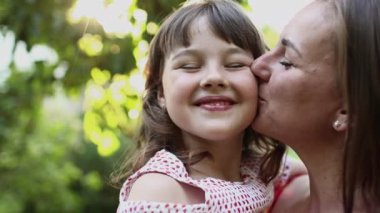 Aile günü, anneler günü. Mutlu gülümseyen genç anne ve sevimli kız çocuğu bahçede sarılıp, öpüşüp, vakit geçiriyorlar. Idyllic ailesi yaz tatilinde dışarıda eğleniyor..
