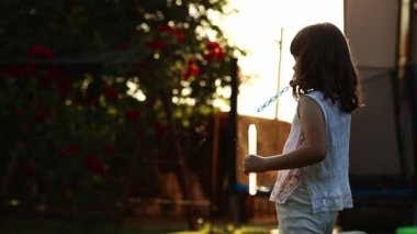 Cheerful playful little girl is blowing soap bubbles, having fun outdoors on backyard on summer warm day. Kid playing on holiday at countryside. Happy children day. Cheerful and carefree childhood.