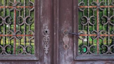 Iron rusty closed door of the lattice gate with forged decorate of ancient building with reflection of the green garden in glass.