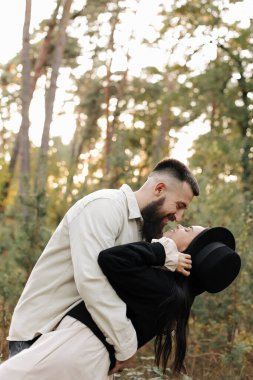 Happy young bearded man with his girlfriend are hugging in the park in warm Valentines day. Loving stylish Heterosexual couple having fun and looking each other on date in nature outdoors