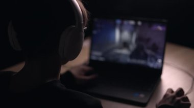 Young gamer is wearing a headset playing FPS video games at home. online video game technology concept. Teen boy play shooter video game on a mouse with a keyboard.Gambling addiction from video games.