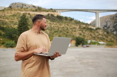 Köprü inşaatında laptopla çalışan sıradan giysili bir adam buldum. Uzaktan kumanda mühendisi ya da serbest çalışan yaşam tarzı kavramı. Hücresel ağ geniş bant kapsama alanı. İnternet 5G.