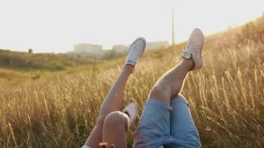 Kadın ve erkek dışarıda eğleniyor. Sevgi dolu hipster çiftler çimenlerde yatar ve gün batımında spor ayakkabılarıyla bacaklarını kaldırırlar. Sevgililer Günü