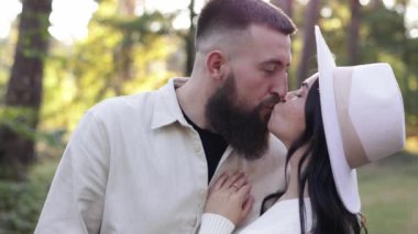 St. Valentines day. Happy stylish loving couple hugging and looking to each others in sunny park. Young bearded man and woman in hat are having date or celebrating anniversary and enjoying nature.