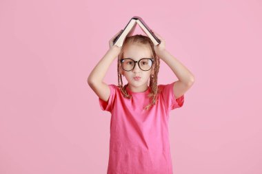 Okul konseptine geri dönelim. Gözlüklü, gülümseyen küçük okul kızı, pembe arka planda izole edilmiş bir çatı gibi kitabı başının üstünde tutuyor. Çocukluk yaşam tarzı konsepti. Okuldaki eğitim. 1 Eylül.