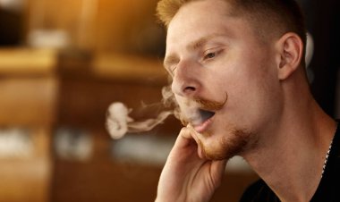 handsome young man with beard and mustache Vaping an Electronic Cigarette. hipster guy Exhaling Smoke Rings