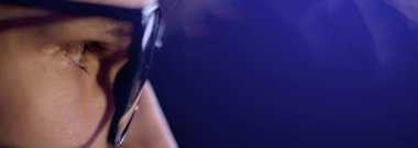 Odaklanmış adamın makro kenarlı gözlüklü görüntüsü karanlıktan gelen ışığa bakıyor. Erkek bilgisayar ekranı, internet, televizyon, akıllı telefon kullanıyor. Okumak, izlemek, geç saatlere kadar çalışmak. Boşluğu kopyala.