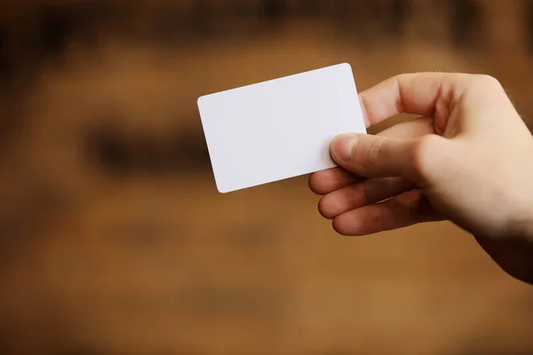 Male hand holds blank white card mockup on brick wall background. Plain call-card mock up template holding arm. Plastic credit namecard display front. Check offset card design. Business branding