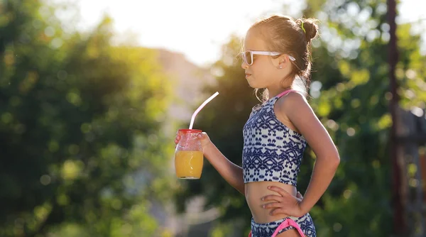 漂亮的小女孩 戴着太阳镜的可爱的蹒跚学步的孩子正在喝橙汁 把大拇指伸出来 穿着泳衣的孩子在靠近游泳池的度假胜地度过了一个愉快的家庭假期 — 图库照片