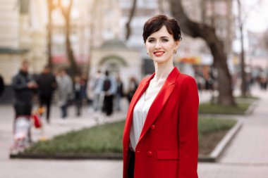 Beautiful confident young woman in a city. Smiling businesswoman in red blazer and red lipstick is looking at camera outdoors. People, business, student lifestyle, city life concept