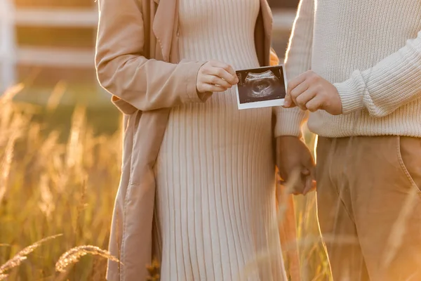 夫との妊娠中の女性の認識されていない日光の中で自然の中で生まれたばかりの子供の超音波スキャン写真を屋外で開催しています 幸せな母親と親の概念 — ストック写真