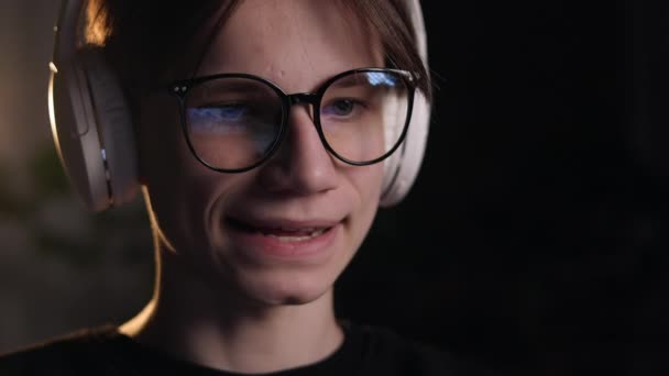 年轻的游戏玩家戴眼镜 带着屏幕反射镜和耳机 一边向订户解释游戏玩法 一边直播动作游戏 黑暗房间里的游戏 Esports Internet和虚拟游戏 — 图库视频影像