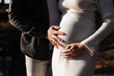 Aile günü. Bebek bekleyen, tanınmayan, şık, evli, hamile bir çift. Adam açık havada kadınların karnına sarılıp dokunuyor. Dünya tüp bebek günü. Hamilelik, ebeveynlik, annelik, aşk, aile kavramı.