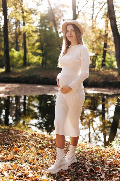 母の日 白いタイトなニットのドレスを着た美しい若い妊婦は 公園内の反射自然と太陽と池で屋外でリラックスし カメラを見ています 女性の日 — ストック写真