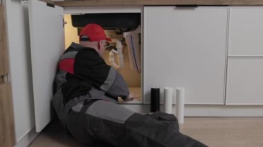 Tulumlu tamirci mutfaktaki lavabonun altındaki içme suyu filtrelerini kuruyor ya da değiştiriyor. Servis konsepti ev filtreleme sistemi. Su kartuşlarının tam zamanında değiştirilmesi sağlıklı bir hayattır.