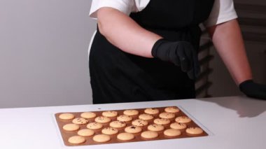 close up of process of making chocolate macarons. chef in black gloves is decorating brown shells of Macaroons and throwing black sesame on it. slow motion video.