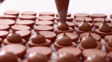 Fransız çöl kurabiyeleri yapıyorum. Pastanedeki kahverengi çikolatalı kurabiyelerin hazır yarımlarına krema ekleyen şefin elleri. yemek, yemek ve pişirme konsepti