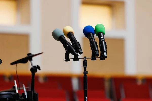 Four coloured microphones on stand on podium and a lot of red chairs blurred in the background. Concept of communication, event, seminar, media, press conference, performance, politics, company