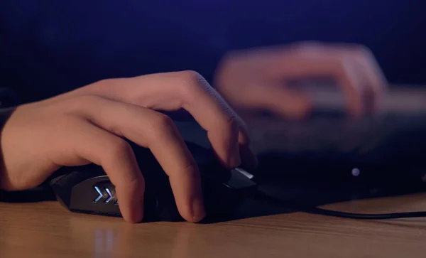 Close up of man gamer hands using computer mouse is playing video game at night. Male hacker breaks into system, coding or data analysis programmer, developer or employee on tech for software code.