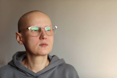 Gözlüklü kel kadın onkolojiyle boğuşuyor. Kemoterapiden sonra kaşlarını ve kirpiklerini kaybeden tüysüz kanser hastası kadın hasta iyileşme sürecinde düşünceli görünüyor. Boşluğu kopyala.