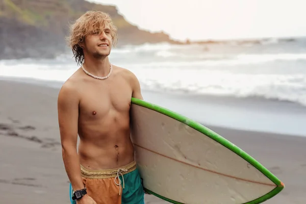 年轻的冲浪手 一头卷曲的金发 带着冲浪板 在海边游玩 玩极端的水上运动 旅行和健康的生活方式概念 体育旅游目的地 — 图库照片
