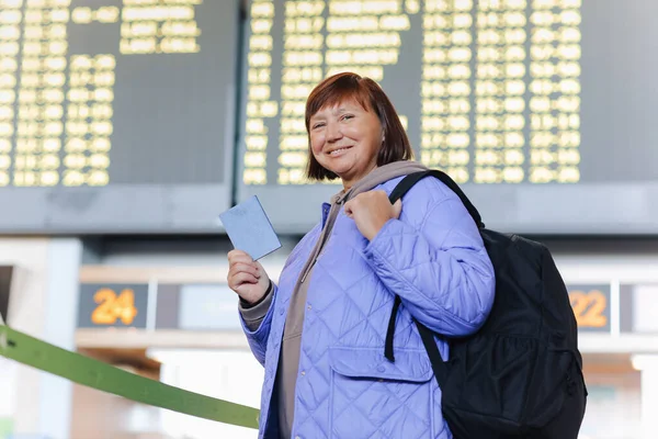 手荷物のある大人の女性旅行者 バックパックはパスポートを保持し 国際空港ターミナルでのフライト旅行を待ちます 中年女性は休暇で外国へ行く 飛行スケジュール — ストック写真