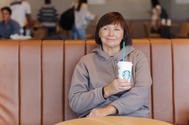 Valencia, İspanya: 18 Mart 2023: Sıradan kıyafetlerle gülümseyen orta yaşlı kadın Starbucks 'taki havaalanındaki Starbucks kahve dükkanında elinde kamışla uçağa binmek için bekliyor..