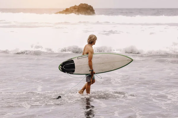年轻的体格健壮的冲浪运动员带着冲浪板跑进大海或海浪中冲浪 极限运动的概念 新的现代生活 体育旅游目的地 — 图库照片