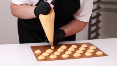 Siyah eldivenli profesyonel kadın aşçı. Makaron tatlısı için temel hazırlıyor. Kurabiye pişirmek için tepsideki boru torbasından hafif krema çıkarılmış. Pişirme, Pişirme kavramı.