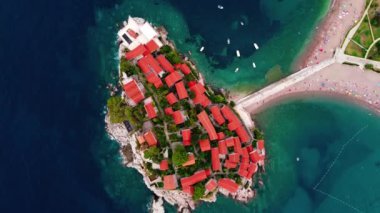 Karadağ 'ın güzel bir yaz gününde Sveti Stefan adası ve kıyılarının havadan görünüşü, insansız hava aracı uçurmaktan. Aziz Stephen 'ın lüks tatil köyünün üstündeki panoramik. Turizm ve eğlence kavramı. Videografi:.