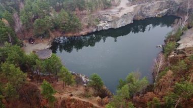 Kuzey Ukrayna 'nın Zhytomyr ilçesinde Korostyshiv granit ocağında bulunan kozalaklı bir sonbahar ormanının ortasındaki zümrüt göl ve kayaların manzarası. Zhytomyr Kanyonu.