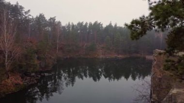 Kuzey Ukrayna 'nın Zhytomyr ilçesinde Korostyshiv granit ocağında bulunan kozalaklı bir sonbahar ormanının ortasındaki zümrüt göl ve kayaların manzarası. Zhytomyr Kanyonu.