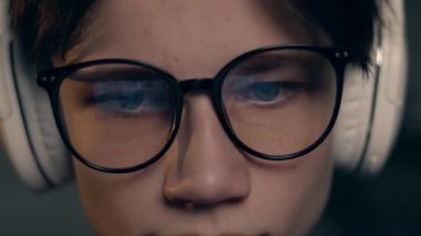 Gözlüklü, ekranda yansıyan ve kulaklıklı genç oyuncu abonelere oyunu anlatırken canlı yayın yapıyor. Karanlık odada oyun, esportlar, internet ve sanal oyunlar.