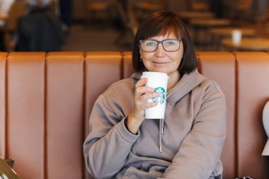 Valencia, İspanya: 18 Mart 2023: Sıradan kıyafetlerle gülümseyen orta yaşlı kadın Starbucks 'taki havaalanındaki Starbucks kahve dükkanında elinde kamışla uçağa binmek için bekliyor..