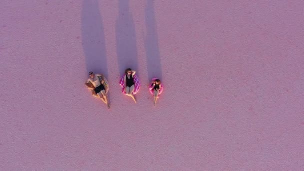 幸せな夏休み 若い家族の空中ビュー お母さん お父さん と子供の娘で水着の上に横たわるインフレータブルフラミンゴとドーナツ上の自然のピンクの塩湖の背景と見てカメラ — ストック動画