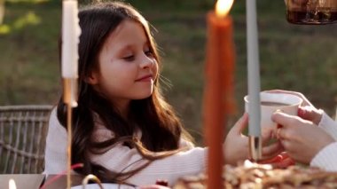 Mutlu aile günleri. Sevimli çocuk annesinin elinden beyaz fincandan sıcak çay içiyor. Şükran Günü şenlik masasında anne ve babasıyla piknikte. Sonbahar parkında mum ve turta yakıyor..