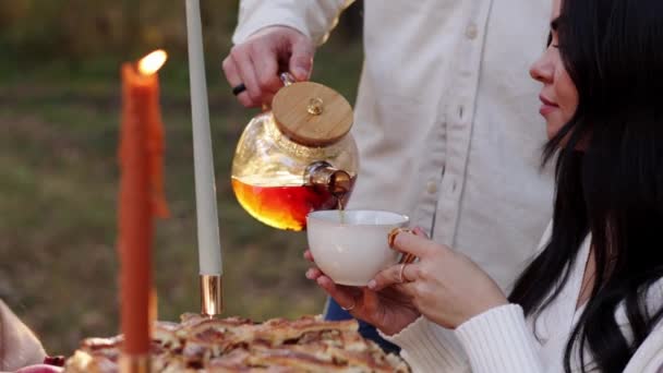 情人节 有爱心的夫妻 男人和女人在秋天的公园里举行浪漫的野餐 并在户外燃着蜡烛 不明身份的男人从透明的茶壶里倒入一杯热饮茶给女孩喝 — 图库视频影像