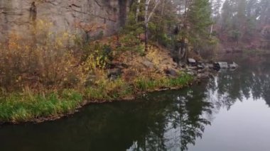 Kuzey Ukrayna 'nın Zhytomyr ilçesinde Korostyshiv granit ocağında bulunan kozalaklı bir sonbahar ormanının ortasındaki zümrüt göl ve kayaların manzarası. Zhytomyr Kanyonu.