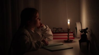 Elektriksiz bir karanlıkta kız öğrenci mesafesini evde öğreniyor. Genç çocuk bilinç kaybı sırasında okul ödevini yapmak için mum ışığını kullanıyor. Enerji krizi konsepti. Ukrayna 'da elektrik kesintisi.